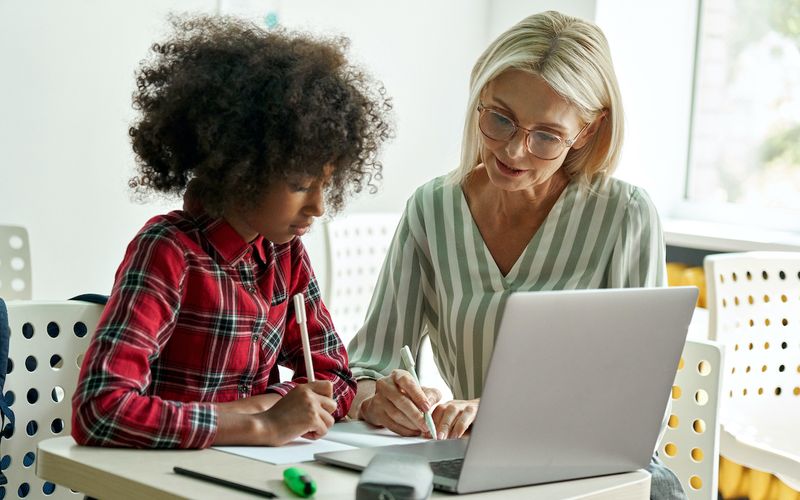 Afro American schoolgirl learning with female tutor teacher using laptop.